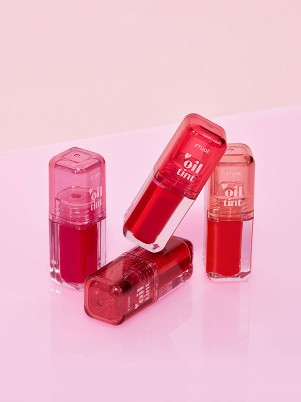 Four red oil tint products on a pink background